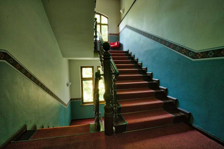 Treppenhaus in einem Altbau mit Holzgeländer, rotem Läufer und Fenster zum Hof
