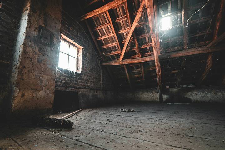 Leerer Dachboden mit Holzbalken, Giebelfenster und Lichteinfall durch das Dach