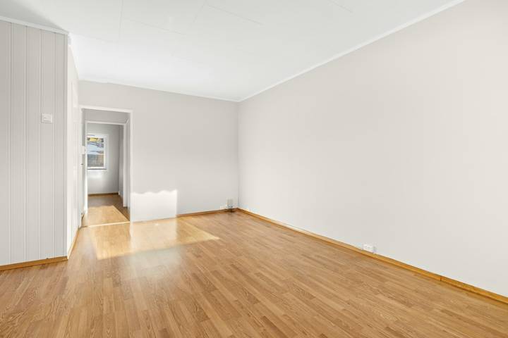Leerer Wohnraum mit Holzboden, weißen Wänden und offener Tür zum Flur