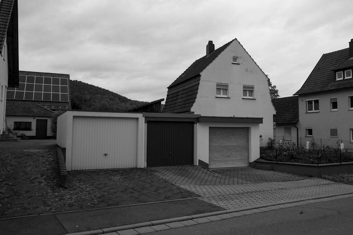 Einfamilienhaus mit drei angebauten Fertiggaragen mit geschlossenen Toren, Schwarzweißfoto