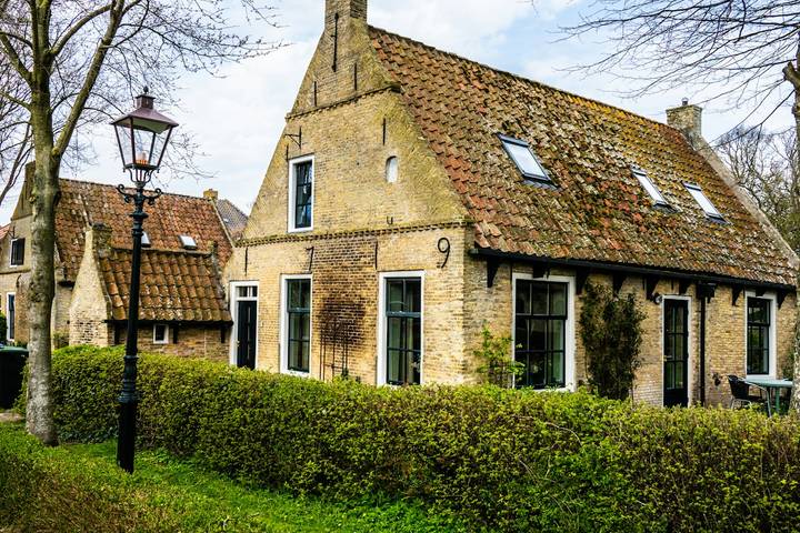 Backsteinhaus mit Dachflächenfenstern im ausgebauten Dach hinter einer Hecke