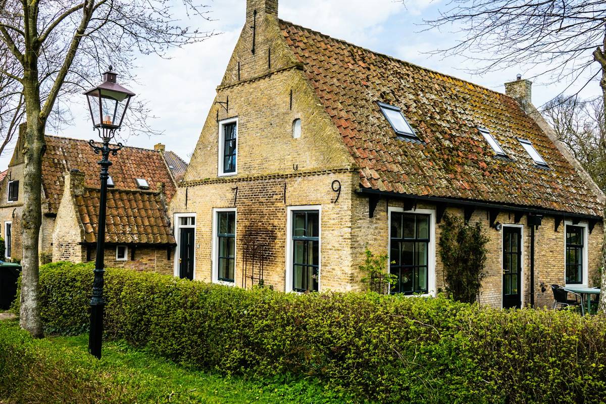 Backsteinhaus mit Dachflächenfenstern im ausgebauten Dach hinter einer Hecke